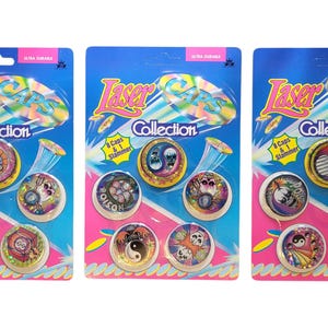 Könnte beinhalten: Drei Packungen der Laser Caps Collection. Jede Packung enthält acht Kapseln und einen Slammer mit runden Designs, darunter Schädel, Yin-Yang-Symbole und abstrakte Muster. Die Verpackung ist blau und rosa, mit dem Text 'Laser Caps Collection'.