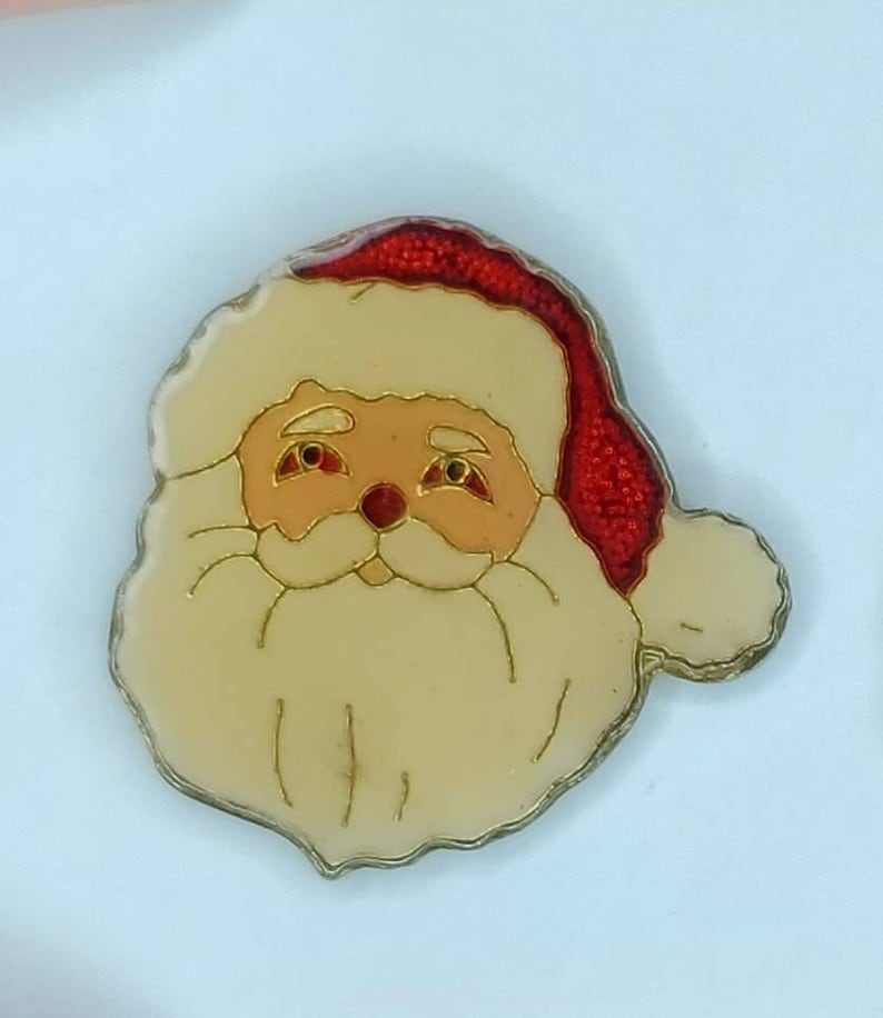 May include: A red and white Santa Claus face ornament with a white beard and a red hat. The ornament is made of glass and has a shiny finish.