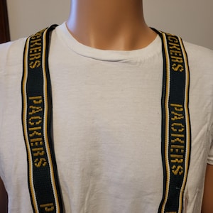 May include: Green and gold suspenders with the word "PACKERS" repeated vertically. The suspenders have metal clips and are displayed against a white background.