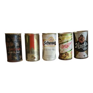 May include: Five vintage beer cans, including Budweiser, Michelob, Schmid, Miller, and Stroh's. The cans show signs of age with rust and wear, showcasing their history. The Schmid can is partially crushed. Each can has unique branding.