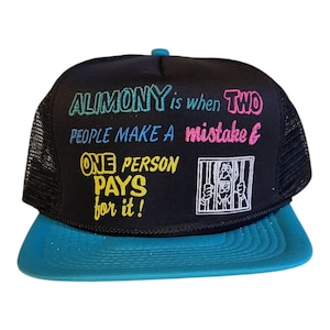 May include: Black trucker cap with a teal peak and mesh back. The cap features the text "ALIMONY is when TWO PEOPLE MAKE A mistake & ONE PERSON PAYS for it!" in colourful lettering, with a cartoon image of a person behind bars.