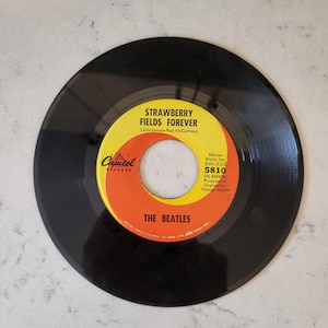 Może przedstawiać: Czarna płyta winylowa z żółto-pomarańczową etykietą. Na etykiecie napis "STRAWBERRY FIELDS FOREVER" zespołu The Beatles. Widoczne logo Capitol Records. Płyta to singiel 7-calowy.