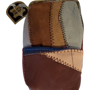 May include: A patchwork leather coin purse with a metal clasp. The purse is made of various leather pieces in shades of brown, beige, blue, and red, stitched together with contrasting thread. A tag that says "GENUINE LEATHER" is attached.
