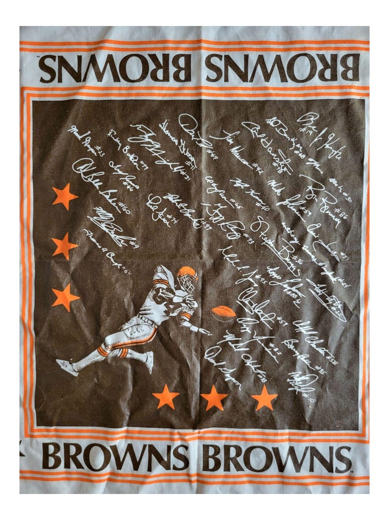 Puede incluir: Toalla del equipo Browns marr&oacute;n y blanca con un jugador de f&uacute;tbol americano, estrellas naranjas y firmas de jugadores. La palabra "BROWNS" est&aacute; impresa en naranja y blanco en los bordes superior e inferior.