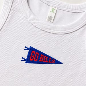 Op de afbeelding: Een wit geribbeld hemdje met een geborduurde blauwe wimpelafbeelding op de borst. De wimpel bevat de rode tekst GO BILLS. Een wit label met maat M is zichtbaar bij de binnenhalslijn, samen met een klein groen rond logolabel.