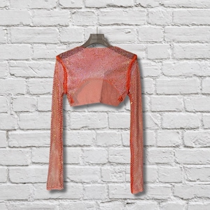 May include: A long-sleeved cropped top made of a shimmering orange mesh material with a fine grid pattern. The garment features a wide neckline and is displayed on a hanger, showcasing a semi-sheer construction with a consistent texture throughout.