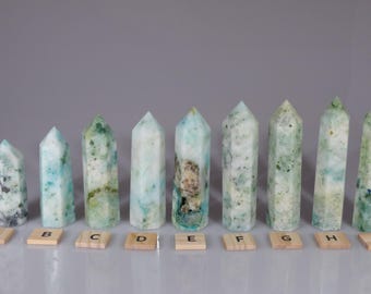 May include: Nine polished green and white crystal points, labeled A through I, arranged in a row on a light gray surface.