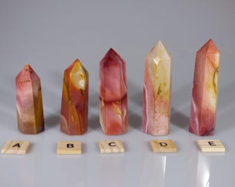 May include: Five polished, multi-colored, crystal point wands, labeled A through E, arranged in a row on a white surface.