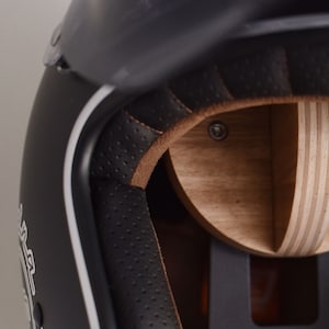 May include: Close-up of the interior of a black motorcycle helmet with a brown leather lining and a wooden shell. The helmet has a white stripe around the edge.