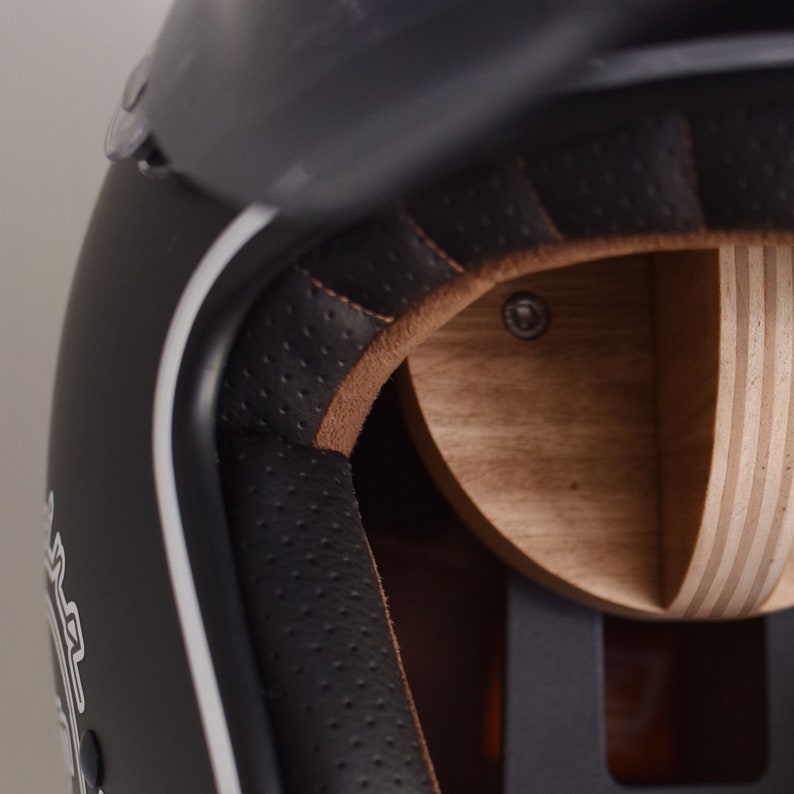 May include: Close-up of the interior of a black motorcycle helmet with a brown leather lining and a wooden shell. The helmet has a white stripe around the edge.