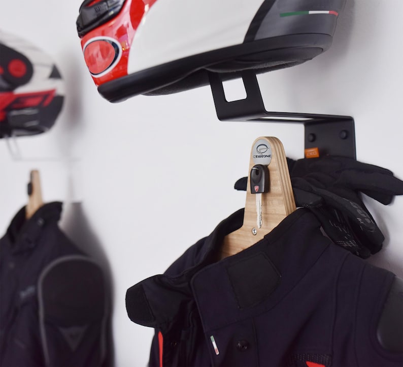 May include: A black metal motorcycle helmet and jacket hanger with a wooden hook. The hook has a key holder and a small logo that says "SHROOMING".