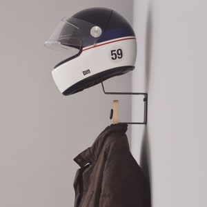May include: A black and white motorcycle helmet with a blue stripe and the number 59 on the side is hanging on a black metal hook. A brown jacket is hanging on a wooden hook below the helmet.