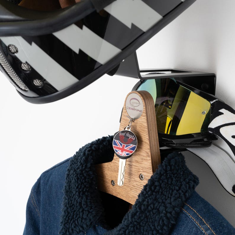May include: A wooden wall-mounted helmet and goggle rack with a black motorcycle helmet, black goggles, and a key with a "Dead Angels" keychain hanging from it. The rack has a black metal base and a wooden top with the word "Overtime" printed on it.