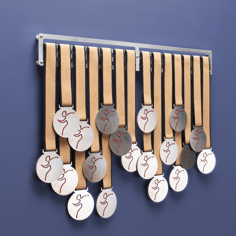 Puede incluir: Un estante de metal plateado con 17 medallas plateadas colgadas. Las medallas tienen un dise&ntilde;o de figura roja corriendo.