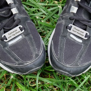 May include: A pair of black sneakers with white accents. The sneakers have metal tags attached to the laces with the text "Customize your tag shoes" and "Choose your text message".