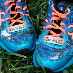 May include: A pair of blue running shoes with a colorful pattern. The shoes have silver metal tags with the text "Mom, You Never" and "Run Alone" on them.