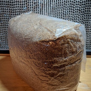 May include: A large, rectangular bag of brown, loose-grain substrate, sealed with clear plastic wrap. The substrate is used for growing mushrooms.