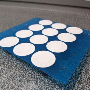 May include: A blue sheet with 12 white round stickers arranged in a grid pattern.