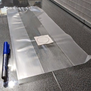 May include: A clear plastic bag with a white circle sticker in the centre. The bag is lying flat on a grey surface.