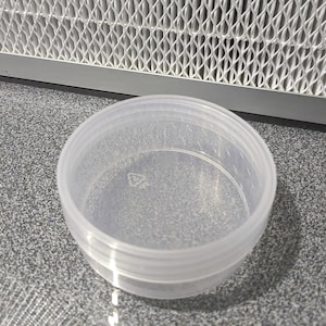 May include: A clear plastic container with a round shape and a smooth surface. The container is made of two pieces that fit together.