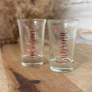 Könnte beinhalten: Zwei klare Schnapsgläser aus Glas mit den Namen "Robin" und "Sabrina" in roségoldener Schrift.