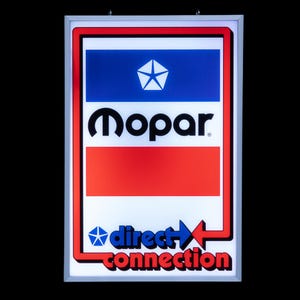Pode incluir: Um letreiro luminoso retangular com moldura prateada, apresentando uma seção superior azul com um logotipo pentastar branco, o texto preto Mopar, uma barra horizontal vermelha central e o texto azul e vermelho direct connection.