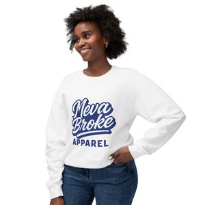 Könnte beinhalten: Weißes Sweatshirt mit dem Text "Neva Broke Apparel" in blauer Schrift. Das Sweatshirt hat lange Ärmel und einen Rundhalsausschnitt. Das Model trägt eine blaue Jeans.