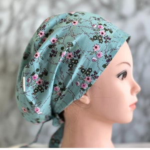 May include: A turquoise blue surgical scrub hat with a pink and green floral pattern. The hat has a tie at the back.