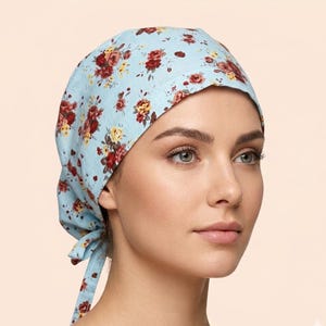 May include: A light blue headscarf with a floral pattern of red and yellow roses. The head covering is tied at the back. The floral pattern is a repeating design. The head covering is made of a soft fabric.