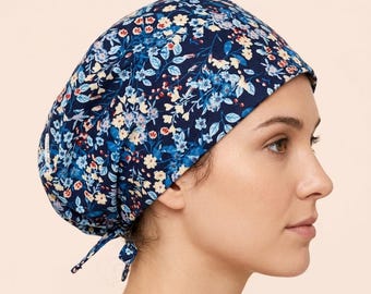 May include: A navy blue scrub cap featuring a dense floral pattern with light blue, white, and soft yellow blossoms and green leaves. The cap has a rounded crown, a wide band, and two fabric ties at the back to secure the fit around the head.