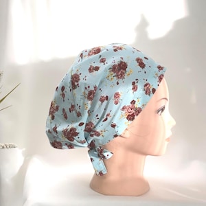 Peut inclure: Un foulard bleu clair orné de motifs floraux. Le tissu présente un motif répété de roses bordeaux et roses avec des accents jaunes. Le foulard est noué à la nuque.