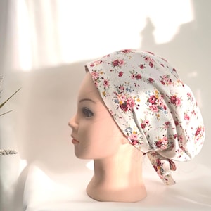 Peut inclure: Un bonnet de chirurgien bouffant à imprimé floral. Le bonnet est blanc avec un motif de fleurs rouges, roses et bleues. Il est noué dans le dos avec un lien en tissu assorti. Idéal pour les environnements médicaux ou esthétiques.