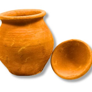 May include: A terracotta clay pot with a matching lid. The pot has a rounded body and a slightly flared rim. The lid is a shallow, rounded dish. The color is a warm, earthy orange.