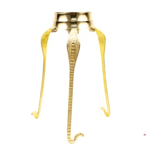 Op de afbeelding: Een goudkleurige metalen standaard met drie poten. De poten zijn gevormd als gestileerde cobra-slangen. De standaard heeft een ronde bovenkant en is ontworpen om een object vast te houden. De standaard wordt waarschijnlijk gebruikt voor religieuze of decoratieve doeleinden.