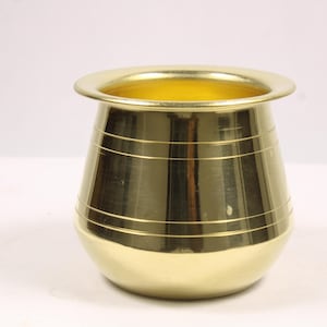 May include: A gold-colored, small, round pot with horizontal bands. The pot has a wide, flat rim and a rounded base. The interior of the pot is a bright yellow color. The pot is made of a shiny metal.