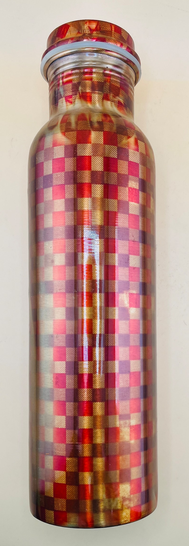 May include: A stainless steel water bottle with a checkered pattern in shades of red, gold, and purple. The bottle has a silver lid and a light blue gasket. The design is reminiscent of a plaid pattern.
