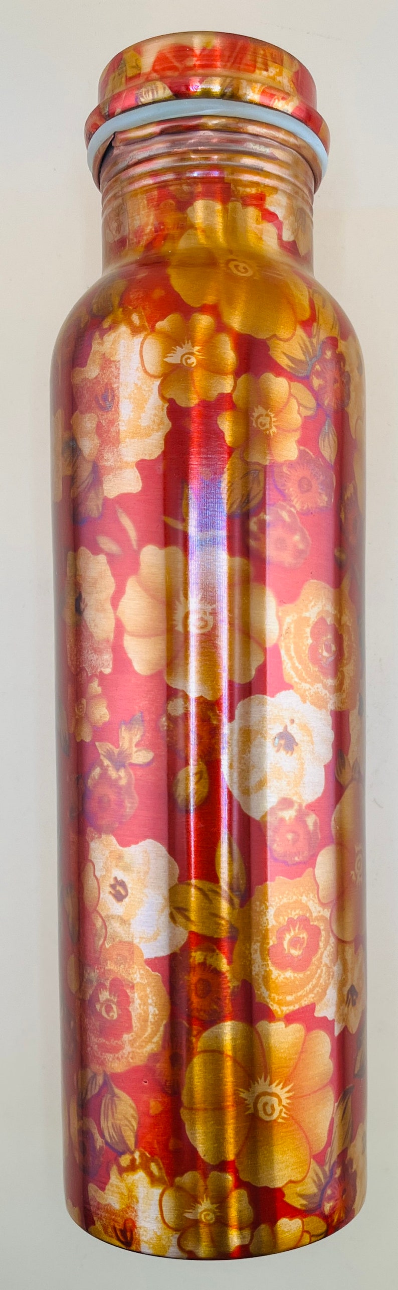 May include: A tall, cylindrical water bottle with a floral design. The bottle has a red background with gold and cream-colored flowers. The lid is a light blue color.