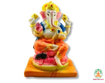 May include: A vibrant statue of Ganesha, the Hindu deity, seated on a lotus flower base. The statue has a white face, pink ears, and orange and blue clothing. Gold accents are on the crown, jewellery, and hands. The base is rectangular, with orange and yellow colours.