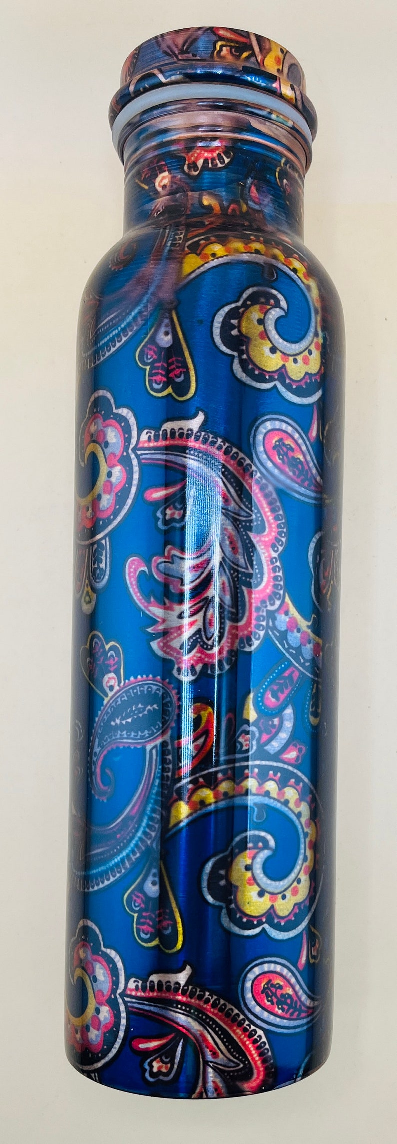 May include: A blue water bottle with a paisley design in red, yellow, and white. The bottle has a shiny, metallic finish and a matching lid. This reusable bottle is great for staying hydrated.