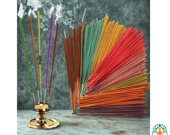 Puede incluir: Una colección de varillas de incienso coloridas, algunas encendidas y emitiendo humo. Un porta incienso dorado está en primer plano, con la palabra "Pooja" visible en una de las varillas. Las varillas de incienso son de varios colores.