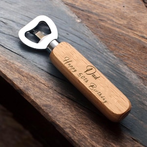 May include: A wooden bottle opener with a silver metal opener. The handle is engraved with the text "Dad Happy 50th Birthday".