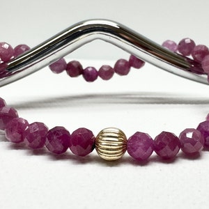 Peut inclure: Un bracelet en pierres précieuses roses avec un accent de perle dorée. Le bracelet est composé de perles facettées et est enfilé sur un élastique.