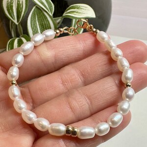 May include: A white pearl bracelet with gold accents. The bracelet is made of small, round pearls and has a gold clasp.