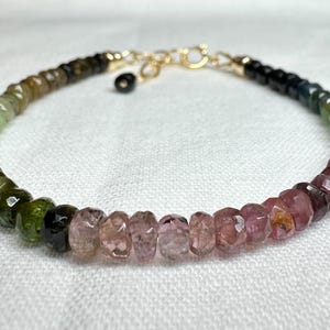 May include: A multi-coloured gemstone bracelet with green, black and pink beads. The bracelet is made with a gold clasp.