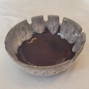 May include: A brown and white ceramic bowl with a scalloped rim. The bowl has a glossy finish and a unique glaze pattern.