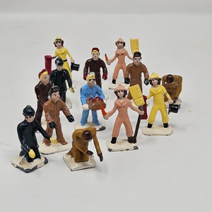 May include: A collection of 12 hand-painted metal figurines, each depicting a different person wearing winter clothing. The figurines are standing on small white bases and are arranged in a semi-circle.