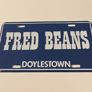 Puede incluir: Placa de matrícula de metal azul y blanco con el texto "FRED BEANS DOYLESTOWN".