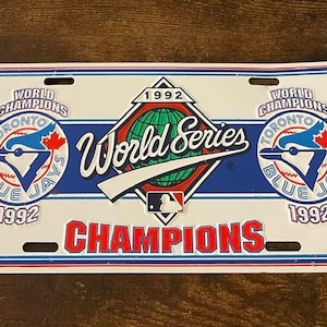 May include: A license plate commemorating the 1992 World Series victory of the Toronto Blue Jays. The plate features the team logo, the words "World Champions," and "World Series" in a red, white, and blue design.