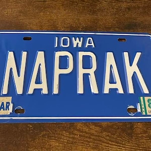 Op de afbeelding: Een blauw en wit kenteken uit Iowa met de naam "NAPRAK" en het nummer "86".