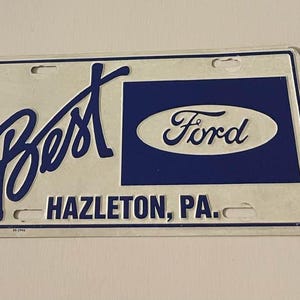 Puede incluir: Placa de matrícula rectangular con las palabras "Best" y "Ford" en letras azules. También se muestra el texto "HAZLETON, PA.". La placa tiene un fondo blanco y un rectángulo azul con el logotipo de Ford.